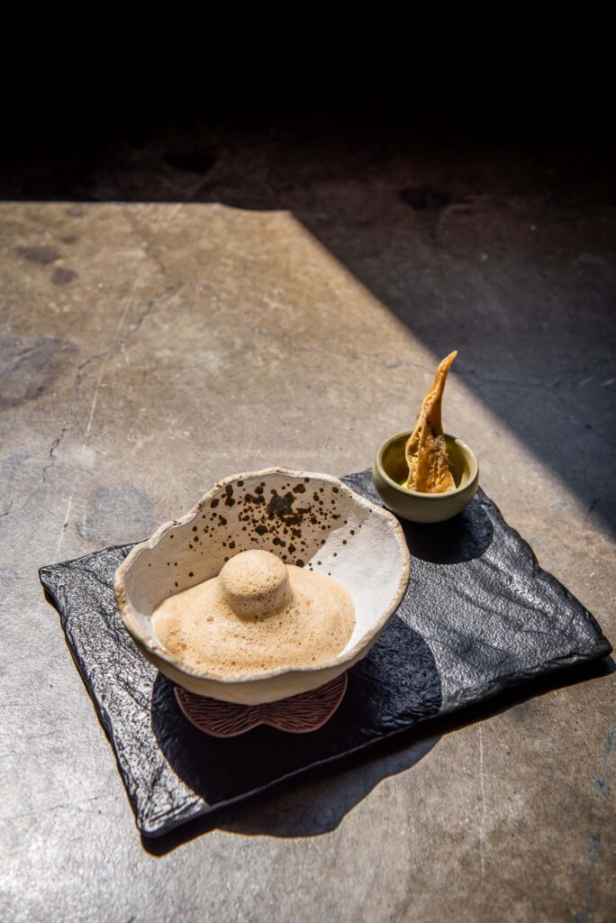 SCALLOP RAVIOLO in tall-walled white dish and black slate serving platter