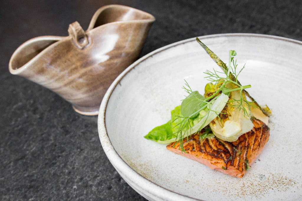 Atlantic salmon served on a grey plate, topped with greens.